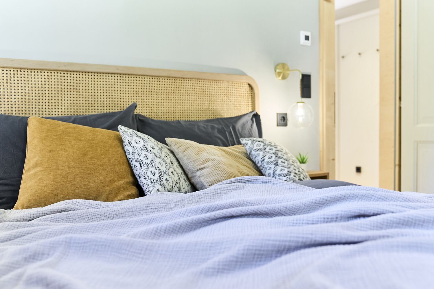 Schlafzimmer mit Rattan-Kopfteil und Kissen in Senf und Blau