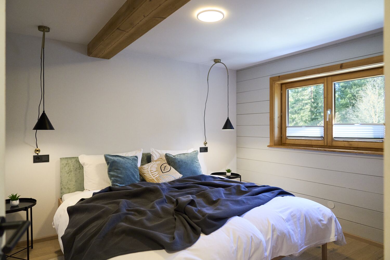 Helles Schlafzimmer mit Pendelleuchten und Fenster ins Grüne