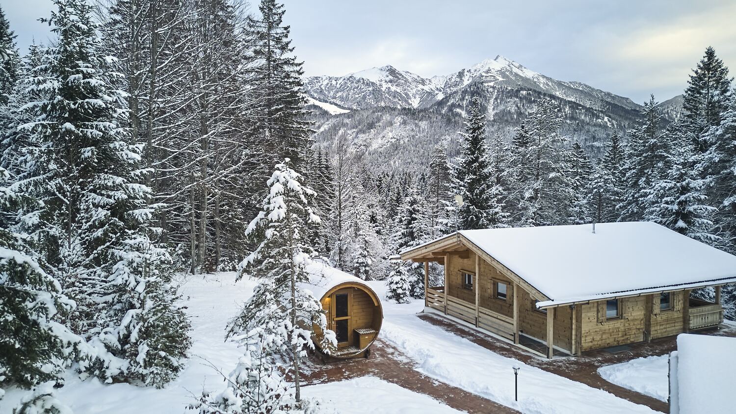 Chalet und Fass-Sauna tief verschneit am Waldrand
